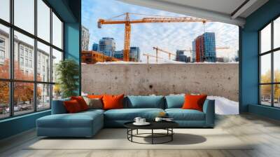 A construction site with cranes amidst snow-covered terrain, framed by modern buildings under a vibrant sky. Wall mural