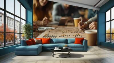 A diverse group of professionals collaborates over charts and coffee, focusing on strategy and data analysis in a cozy workspace. Wall mural