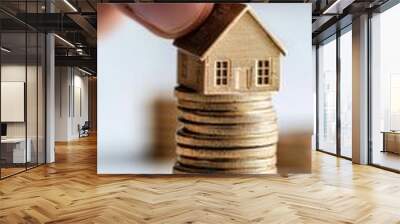 A hand placing a miniature house on a stack of gold coins, symbolizing investment, wealth, and real estate market concepts. Wall mural