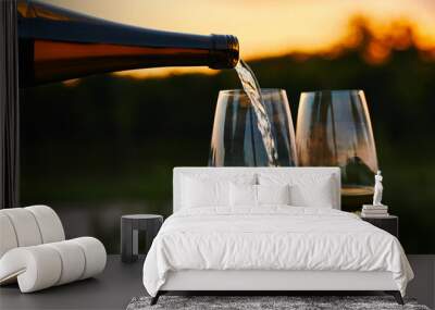 Pouring white wine into glasses in the vineyard at sunset Wall mural