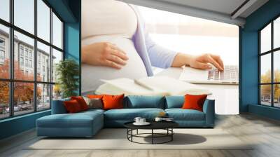 Pregnant woman working on laptop at home Wall mural