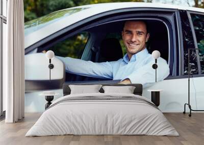 Smiling young man sitting in his car Wall mural