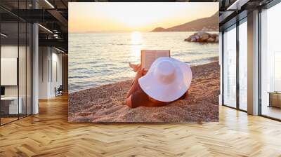 Woman reading a book on the beach at sunset Wall mural