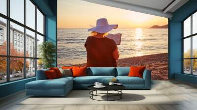 Woman reading a book on the beach at sunset Wall mural