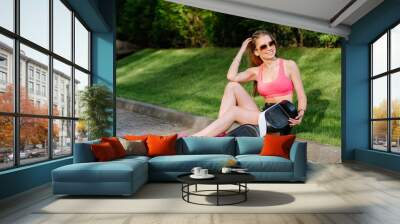 Young pretty woman in shorts and top sitthing with hoverboard on the green grass Wall mural