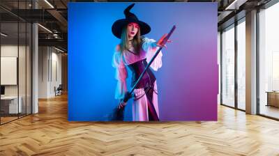 a girl in a witch costume for Halloween with a broom and a pumpkin in neon light Wall mural