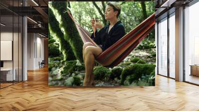 A pretty girl with short hair in a hammock in the forest catches smoking a pipe with marijuana Wall mural