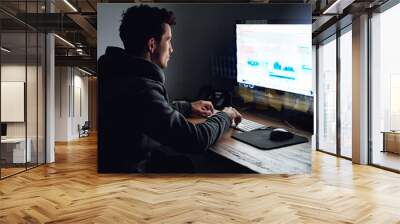 Binary is his second language. Rearview shot of a young programmer working on his computer late at night. Wall mural