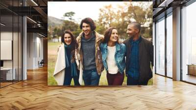 Where are we going to now. Portrait of a group of cheerful young friends huddled together while walking in a park outside during the day. Wall mural