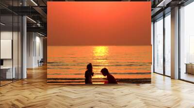 Silhouettes of two children playing on the beach against the sun Wall mural