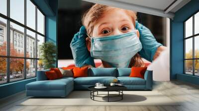 Mother puts on her baby sterile medical mask. Little girl and mom in medical mask. vaccination of children Wall mural