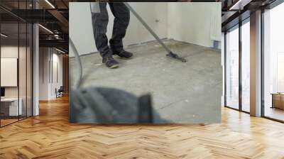 Man in denim pants. Performs cleaning of production facilities. Apartment after renovation with a vacuum cleaner. A worker vacuums a room after repairing the floors. Wall mural