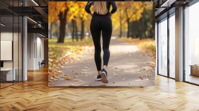 Rear view of a young athletic woman in black sportswear who is jogging early morning in the autumn park Wall mural