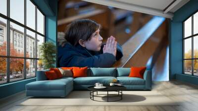 a little boy in a jacket prays in a dark catholic church at a children's mass Wall mural