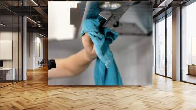 Woman wiping exhaust hood in kitchen, closeup. A woman's hand washes the hood in the kitchen with a rag. Cleaning a household hood. Female hands cleaning a kitchen hood with a cloth. Wall mural