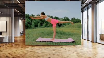 young white woman with dark hair and a short haircut in a white top and leggings does yoga in nature at sunset Wall mural