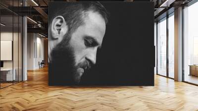 beautiful pensive mindful young trendy caucasian strong man with beard looking down side on black background with copy space Wall mural