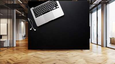 Laptop and earbuds on dark, black desk Wall mural