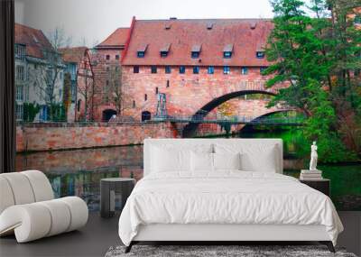  Schlayerturm tower and Kettensteg Chain Bridge over Pegnitz river in Nuremberg, Bavaria Germany. Bridge spans a river with a brick building in the background Wall mural