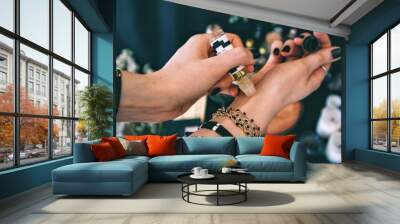 Female applying essential oil on her wrist. Caucasian woman wearing bracelets jewelry and black nail polish. Emerald green dark themed color palette. Essential oil on left hand, applying on right hand Wall mural