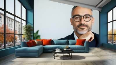 Confident professional in glasses, wearing a tailored suit, thoughtful expression with hand on chin, modern office background with greenery, conveying success and intellect Wall mural