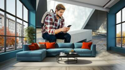 Portrait of modern young man with smartphone on a street Wall mural