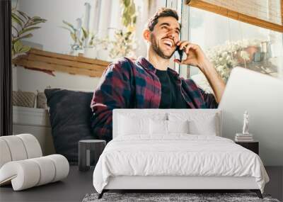 Young man with laptop and smartphone at home. Freelancer. Concept of remote work or study. Wall mural