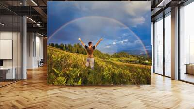 A happy man enjoys the rainbow in the mountains. Wall mural