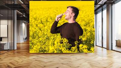 man in yellow canola field blowing his nose and suffering from pollen allergy. Wall mural