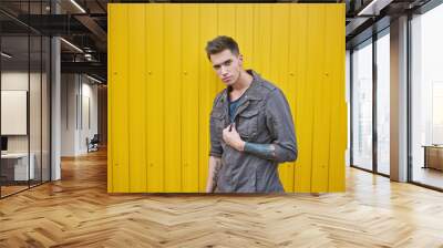 Young fashion guy in a denim jacket, stands near the yellow wall Wall mural