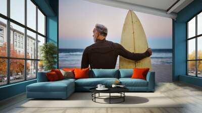 Beach, man and surfboard with back view for morning cardio fitness and tranquil swim in nature. Senior surfer waiting for low tide at ocean for calm surf waves with peaceful sky at dawn. Wall mural