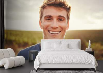 Happy, face and nature with a man at sunset, enjoying freedom with a smile and standing on a field of grass in the day. Travel, vacation and morning with the portrait of a handsome young male outside Wall mural