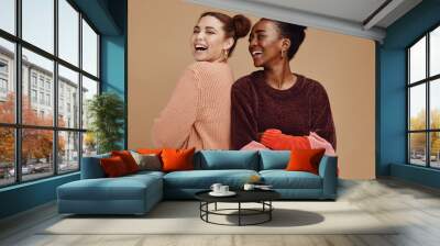 Happy, smile and women friends in a studio together with fun, freedom and positive mindset. Happiness, excited and interracial girl best friends smiling with style while isolated by brown background. Wall mural