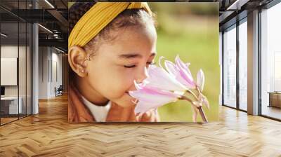 Nature, beauty and child smell flower in park, enjoying weekend, holiday and vacation in countryside. Peaceful, freedom and young black girl smelling aroma or scent of plant on field in spring time Wall mural