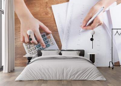 young woman counts on calculator and makes notes on papers Wall mural