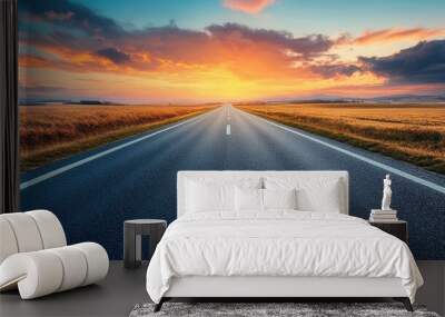 A long, straight road stretching into the distance at sunset, with the sky ablaze in warm colors and the sun casting long shadows across the pavement. Wall mural