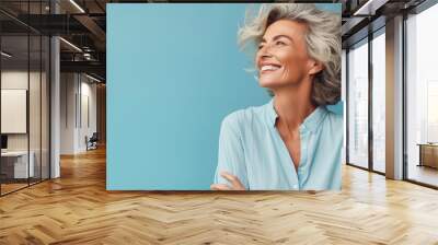 Against a pastel blue canvas, a mature woman exudes carefree vibes in a waist-up portrait. Her relaxed demeanor and joyful expression convey a sense of freedom and happiness Wall mural