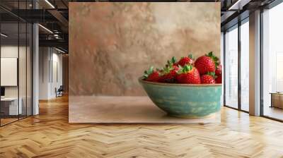 A blue ceramic bowl filled with red ripe strawberries, sitting on a light brown textured surface. Wall mural