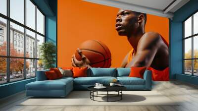 A man in an orange basketball jersey holds a basketball against an orange backdrop. Wall mural