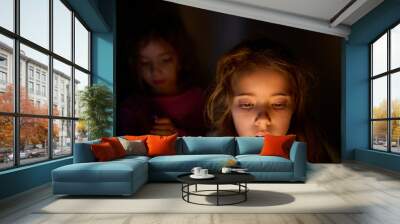 2 girls playing in a dimly lit room. The older one is illuminated by a pint intense light Wall mural