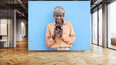 Beautiful mature african woman looking on smartphone while wearing headphones - Elderly generation enjoy technology Wall mural