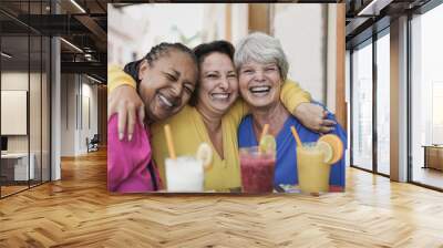 Multiracial senior women taking a selife at bar terrace - Elderly girlfriends enjoy healthy smoothie and smiling on camera Wall mural