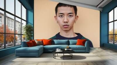 Young asian boy looking serious on camera with yellow wall in background Wall mural