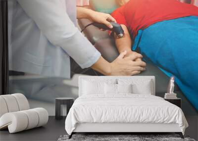 Selective focus on hand of male physiotherapist using ultrasound head for treatment on tennis's elbow syndrome, rehab room on the background in hospital Wall mural