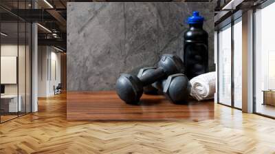 A pair of vintage iron dumbbells with a water bottle and white towel on a wooden floor and a cement wall. Wall mural