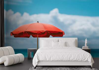 A vibrant red beach umbrella stands against a clear blue sky by the ocean in summer Wall mural