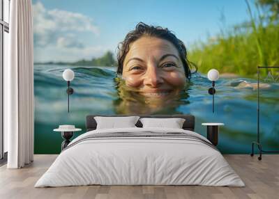 A woman enjoying a tranquil swim in a clear lake surrounded by lush greenery on a sunny day Wall mural