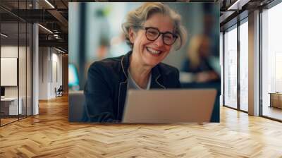 Happy lady wearing spectacles at desk with laptop Wall mural