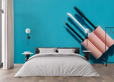 pink brushes for cosmetics, mascara, liquid lipstick, eyeliner, lip gloss on a blue background, copy space Wall mural