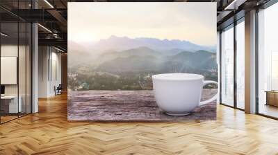 A white cup of hot espresso coffee mugs placed on a wooden floor with morning fog and moutains with sunlight background,coffee morning Wall mural